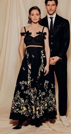 a man and woman standing next to each other in front of a white backdrop wearing formal clothes