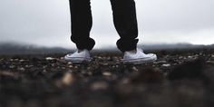 a person standing in the middle of a field with their legs crossed and white sneakers on