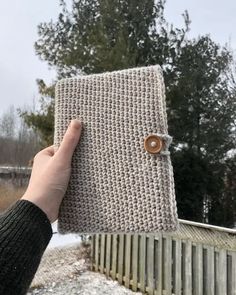 a person holding up a crocheted book with buttons on the front and side