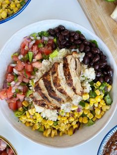 a white bowl filled with chicken, rice and beans next to other bowls of vegetables