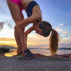 a woman in pink shorts and blue top doing a handstand on the beach