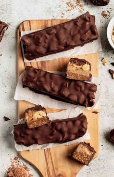 three pieces of chocolate peanut butter bars sitting on top of a cutting board next to some nuts