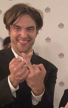 a man in a suit and tie smiling at the camera with his hands clasped together