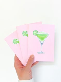 a hand holding three cards with limes on them and one has a green drink in it