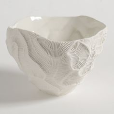 a white bowl with an intricate design on the outside and inside, sitting on a white surface