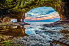 an ocean cave with the sun setting in the distance and water reflecting it's surface