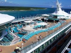 people are walking on the deck of a cruise ship near an outdoor pool and water slide