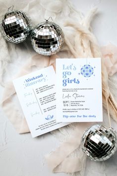 three disco ball ornaments sitting on top of a sheet of paper next to some feathers