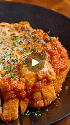 chicken parmesan on a black plate with bread and parsley sprinkled