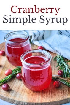 cranberry simple syrup in jars on a cutting board with rosemary sprigs