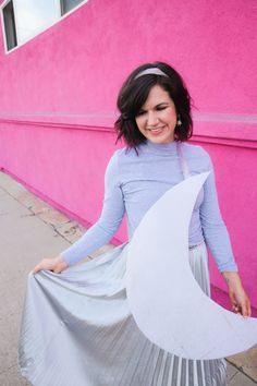 a woman in a blue shirt and silver pleated skirt holding a large white piece of paper