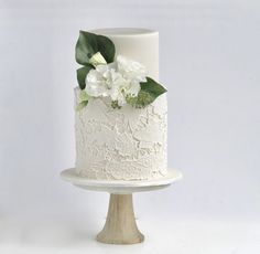 a white wedding cake with flowers and leaves on the top is sitting on a wooden stand