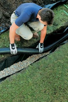 a man is working on a drainage system in the grass with his hands and gloves