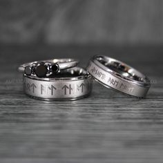 two wedding rings with black stones are on a wooden surface, one has an arrow and the other is engraved