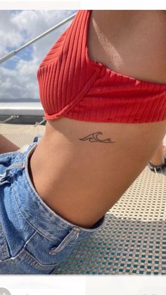 a woman with a small wave tattoo on her lower back ribcage, sitting on the beach