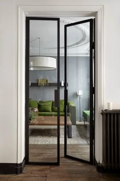 an open door leading to a living room with green couches and lamps on the wall