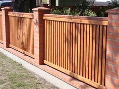 a brick fence with wooden slats on the top and bottom, in front of a house