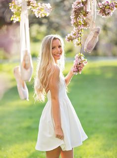 a woman in a white dress is holding flowers and hanging from a tree with shoes on it