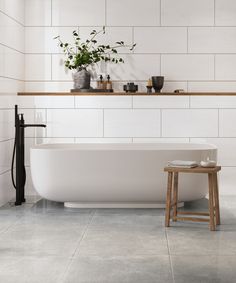 a white bath tub sitting in a bathroom next to a wooden stool and potted plant