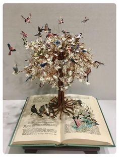 an open book with butterflies flying out of the pages and on top of it is a tree