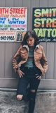 a woman leaning against a wall in front of a tattoo parlor with her hands on her hips