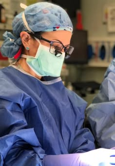 a woman in scrubs and goggles is performing surgery on her hand while looking at the camera