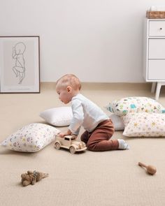 a baby playing with toys on the floor next to pillows and stuffed animals in a bedroom