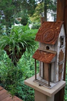 a bird house sitting on top of a cement block next to a tree and bushes