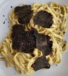 a white plate topped with pasta covered in cheese and black trufflette toppings