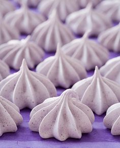 there are many small white desserts on the purple tablecloth, one is frosted with icing and the other is decorated with sprinkles