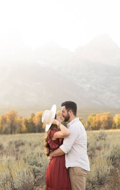 a man and woman standing next to each other in a field with mountains behind them