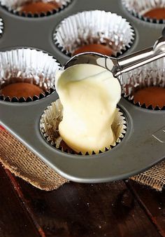 cupcake batter being poured into a muffin tin filled with brownies and white frosting