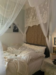 an unmade bed with sheer curtains and white linens on the headboard, in a bedroom