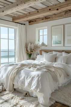 a bed with white linens and pillows in a bedroom next to the ocean on a sunny day