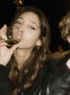 a woman drinking from a wine glass next to a man in a leather jacket and red shirt