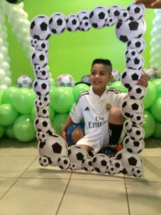 a young boy sitting in front of a photo frame with soccer balls on it