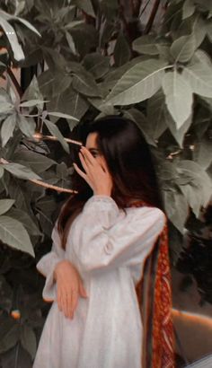 a woman standing in front of a tree with her hand on her face