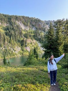 a woman is standing on a trail pointing at the water and mountains in the background