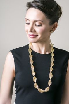 a woman wearing a black top and gold necklace with an intricate design on the front