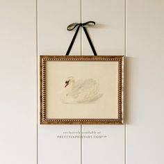 a white swan is hanging on the wall next to a frame with a black bow