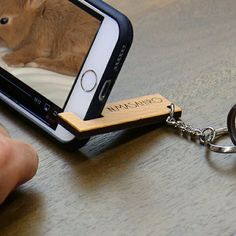 a person holding a cell phone with a wooden keychain attached to it and a rabbit on the screen