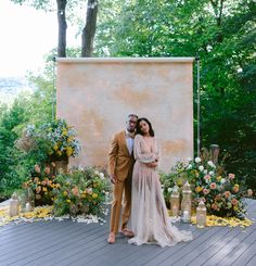 a man and woman standing next to each other in front of a wall with flowers