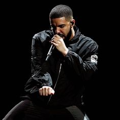 a man sitting on top of a stool holding a microphone to his mouth while wearing a black jacket