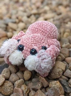 a pink stuffed animal sitting on top of some rocks and gravel with eyes wide open