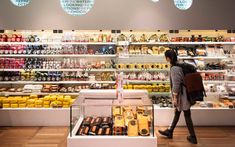 a woman walking past a store filled with lots of food and drink bottles on shelves