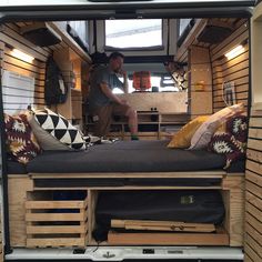 a man sitting on top of a bed in the back of a truck with wooden pallets