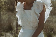 a woman wearing a white wedding dress with ruffles on the shoulders and neck