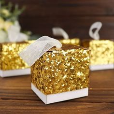 two small boxes with gold glitter on them sitting on top of a wooden table next to flowers