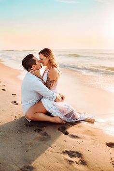 a man and woman are sitting on the sand at the beach, hugging each other