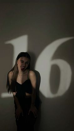 a woman standing in front of a wall with the number fifteen six projected on it